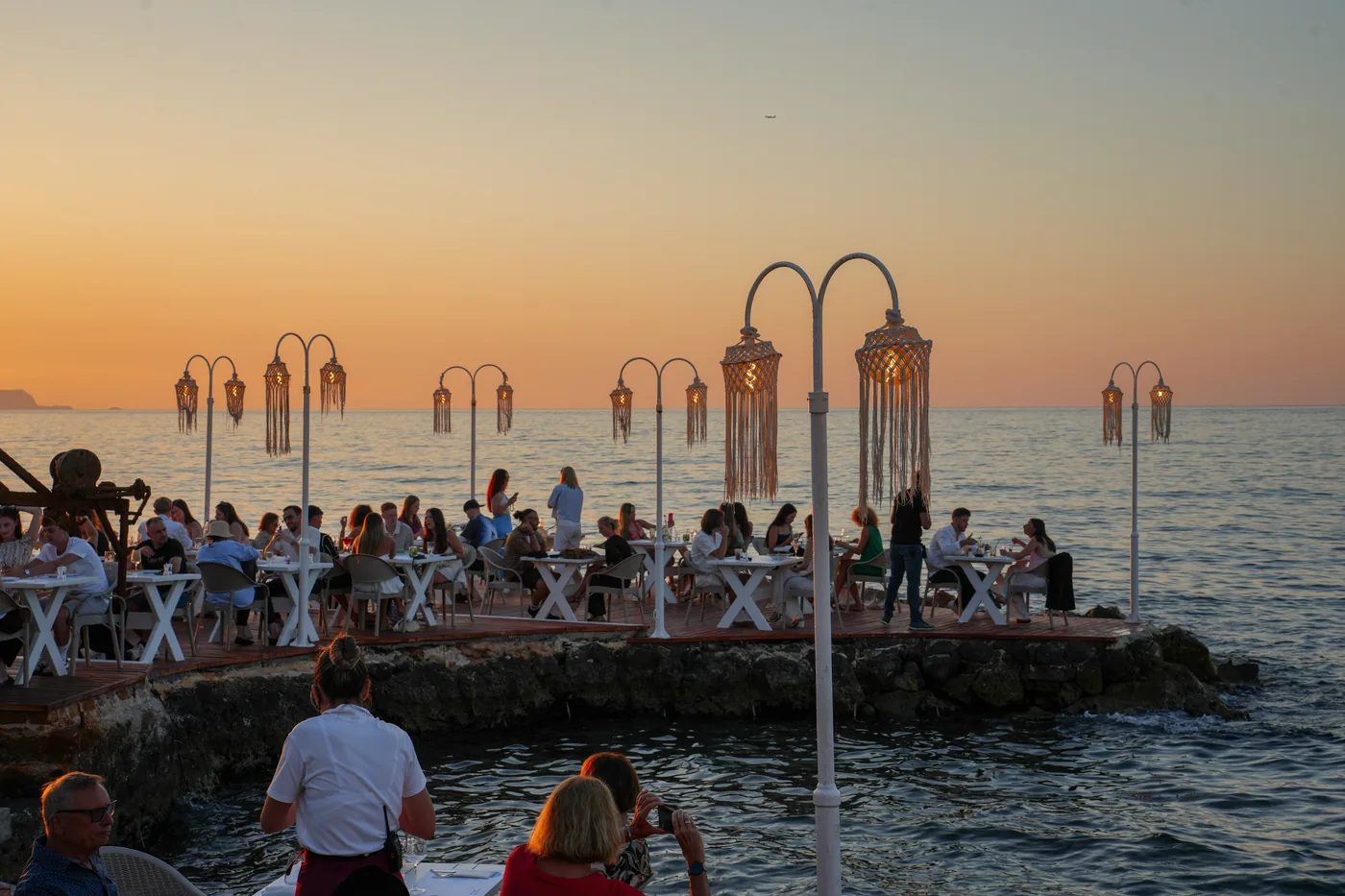 Waterfront dining tables beneath Thalassa’s lanterns at sunset